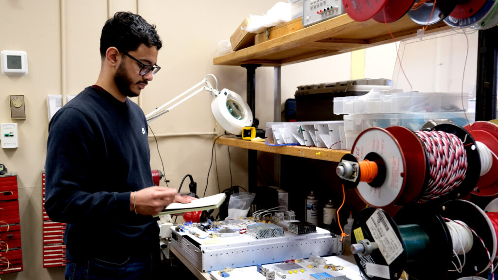 a man holding a notebook and looking at a box of wires and technical components