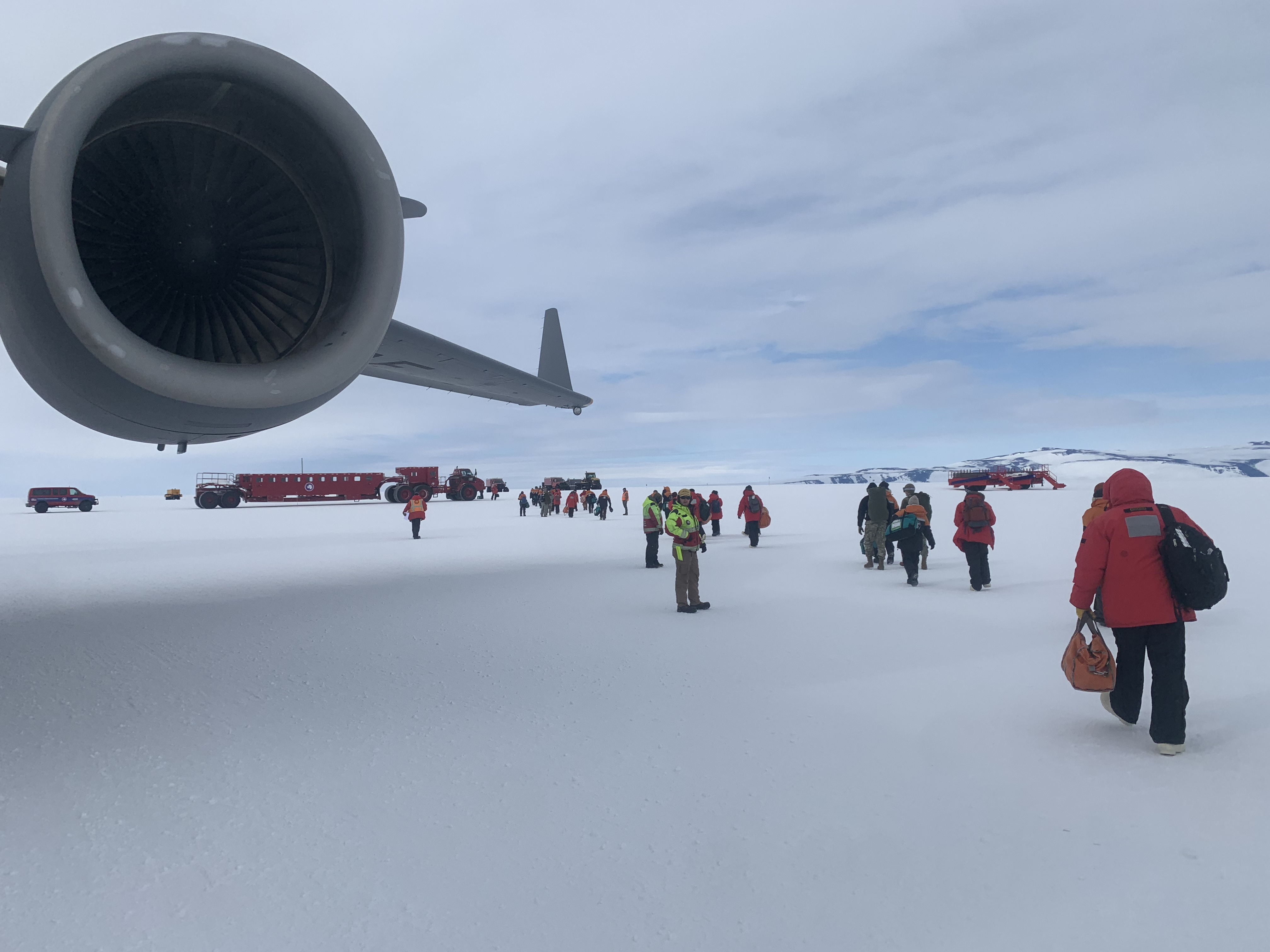 A plane's jet engine next to people walking to board the plane