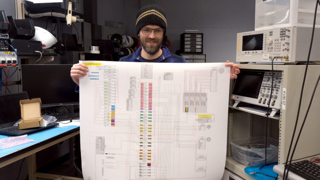 A man holding a poster showing a detailed electrical engineering schematic of the hub enclosure box